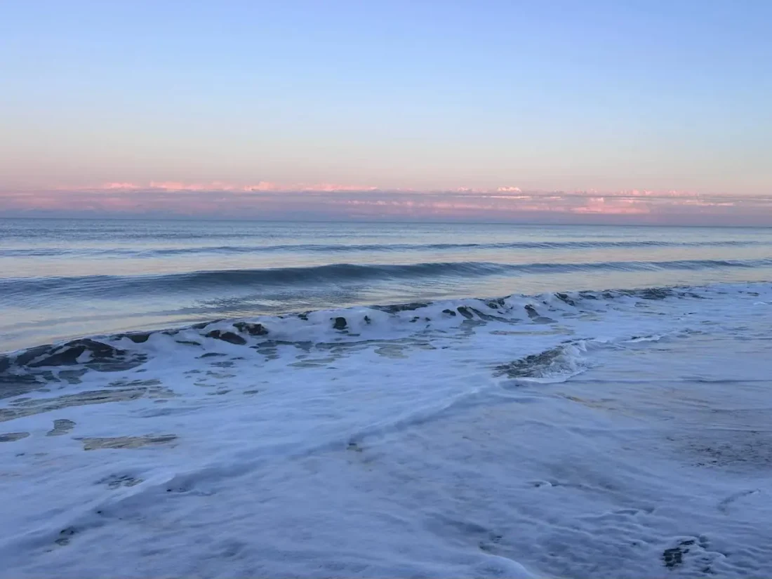 A gentle wave washing onto a pale sandy beach at dawn