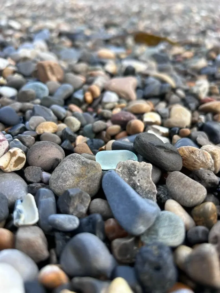 A pale blue sea glass fragment resting among shoreline stones